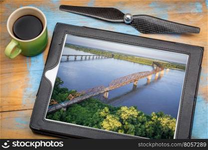 aerial landscape photography concept - reviewing aerial pictures of old and new Chain of Rocks Bridge over Mississippi RIver on a digital tablet with a drone propeller and coffee, screen picture copyright by the photographer