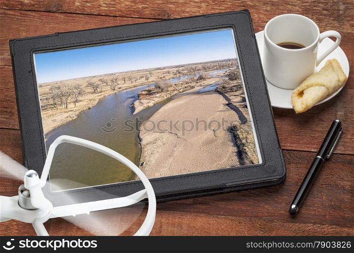 aerial landscape photography concept - reviewing aerial pictures of the South Platte RIver in Colorado on a digital tablet with a drone rotor and cup of coffee, screen picture copyright by the photographer