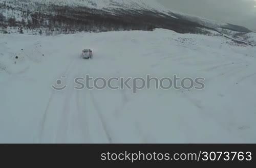 Aerial - offroader driving on snowy road on dull cloudy day. Car traveling in the mountains in winter