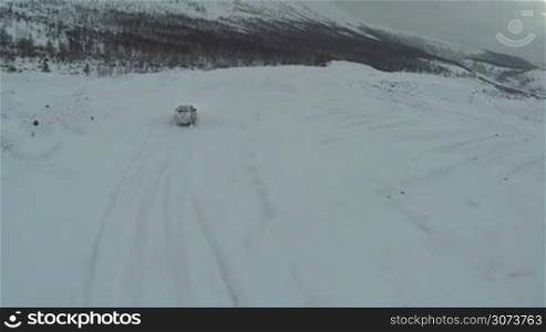 Aerial - offroader driving on snowy road on dull cloudy day. Car traveling in the mountains in winter