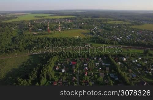 Aerial panorama of countryside with summer houses among green woods and moving cargo train, Russia
