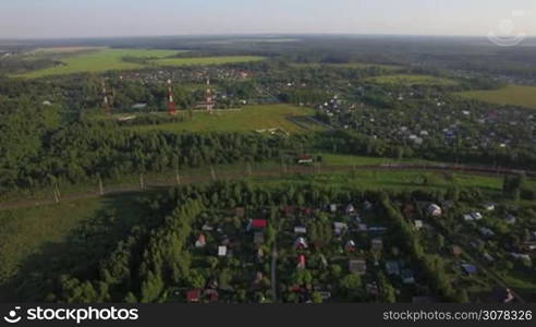 Aerial panorama of countryside with summer houses among green woods and moving cargo train, Russia