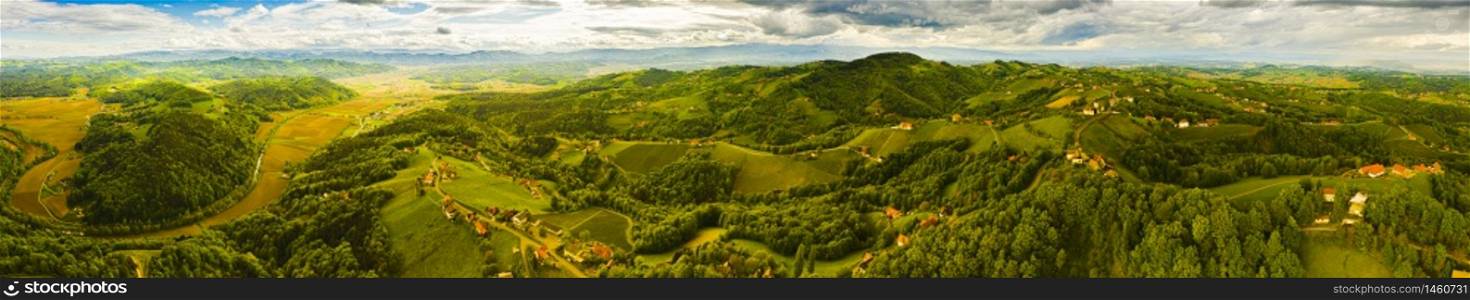 Aerial panorama of of green hills and vineyards with mountains in background. Austria vineyards landscape. Leibnitz area in south Styria, wine country. Tuscany like place and famous tourist spot. Aerial panorama of of green hills and vineyards with mountains in background