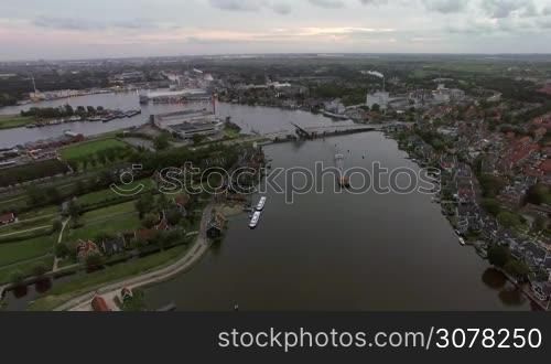 Aerial panorama of town in Netherlands. Private houses, green areas and river with sailing barge