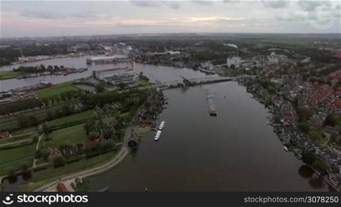 Aerial panorama of town in Netherlands. Private houses, green areas and river with sailing barge