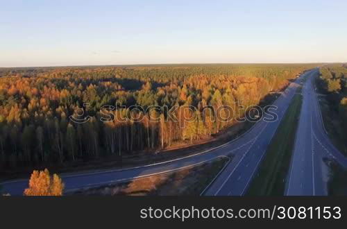 Aerial panoramic of a highway with traffic among a mixed hardwoods and conifer forest at sunset