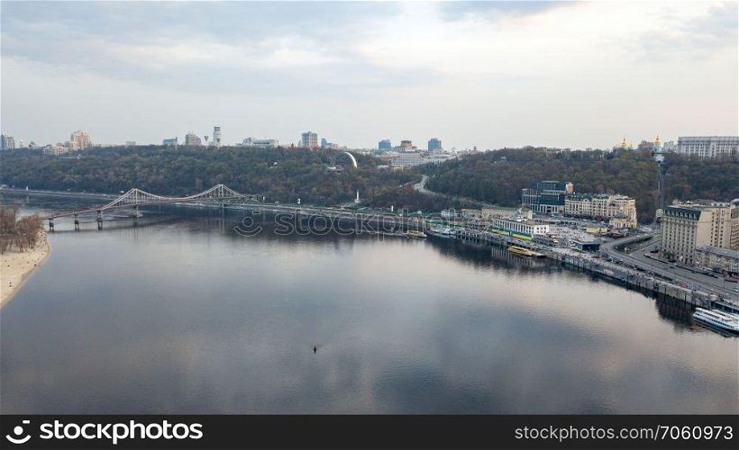 Aerial panoramic view from the drone on the central historical part of the city Kiyv, and the district of Podol with the Postal square, hotels, churches, river Port. Reflection of sunset and cloudy sky in the Dnieper River.. The panoramic bird&rsquo;s eye view shooting from drone of the Podol district, the right bank of the Dnieper River and centre of Kiev, Ukraine summer evening at sunset on the background of the cloudy sky.