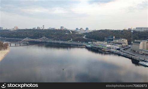Aerial panoramic view from the drone on the central historical part of the city Kiyv, and the district of Podol with the Postal square, hotels, churches, river Port. Reflection of sunset and cloudy sky in the Dnieper River.. The panoramic bird&rsquo;s eye view shooting from drone of the Podol district, the right bank of the Dnieper River and centre of Kiev, Ukraine summer evening at sunset on the background of the cloudy sky.
