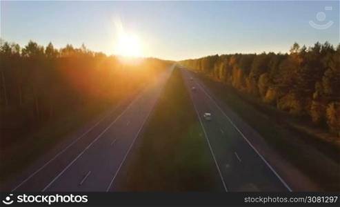 Aerial panoramic view of a highway with traffic along a mixed hardwoods and conifer forest at sunset
