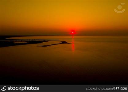 Aerial photo from flying drone of a fascinating nature landscape with dramatic evening sunset sky which reflected in sea water with calm waves. Beautiful scenery of a Indian Ocean with sunrise