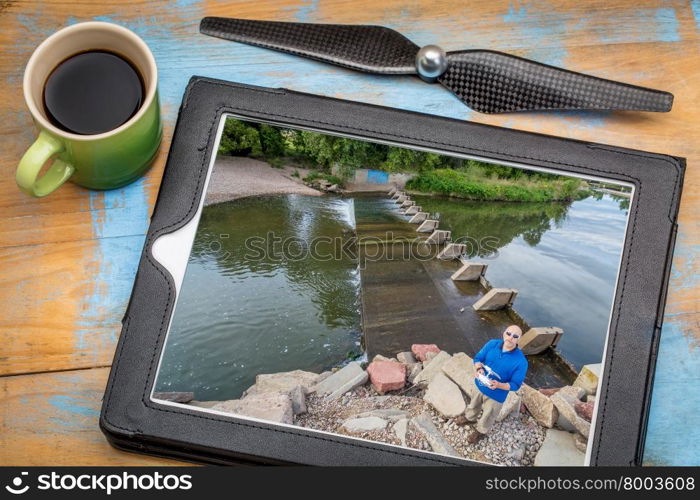 aerial photography concept - reviewing aerial picture (drone operator on a river shore) on a digital tablet with a drone rotor propeller and a cup of coffee