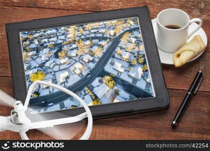 aerial photography concept - reviewing aerial pictures of city residential area in snow on a digital tablet with a drone rotor and coffee, screen picture copyright by the photographer