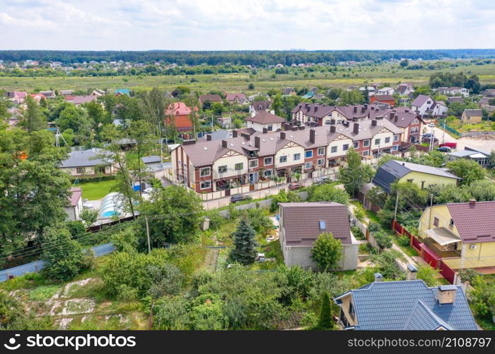 Aerial photography of residential areas of the suburbs overlooking new two-story townhouses, aerial view, photographing the village against the backdrop of green fields and blue sky. Copy space.. Aerial photography, suburban residential areas on a summer day, two-story townhouses amid country houses and fresh green vegetation.