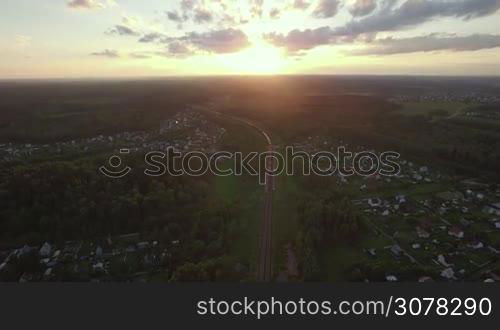 Aerial rural scene with village and freight train running through it at sunset, Russia