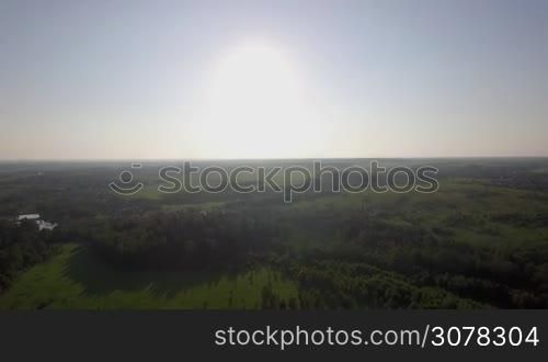 Aerial scene of countryside in bright sunlight. Russian landscape with green woods, fields and village