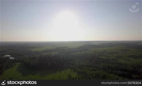 Aerial scene of countryside in bright sunlight. Russian landscape with green woods, fields and village