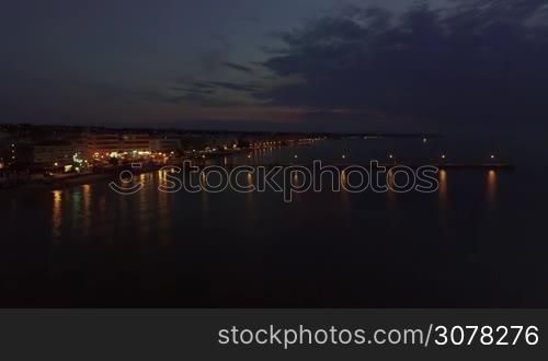 Aerial scene of resort at night. Quiet sea, pier with people and coastline illuminated with lanterns. Thessaloniki, Greece