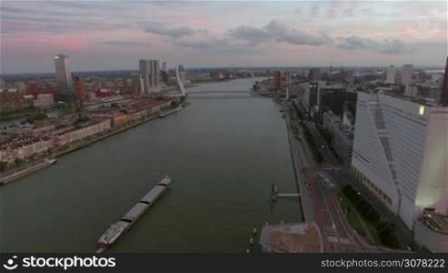 Aerial scene of Rotterdam with Erasmus Bridge, city buildings and ship sailing along the river. View in the evening, Netherlands