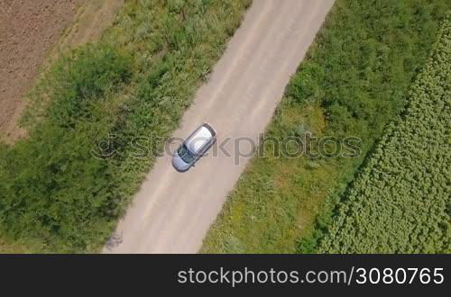 Aerial shot from top of car vehicle driving on countryside road with fields on both side.