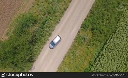 Aerial shot from top of car vehicle driving on countryside road with fields on both side.