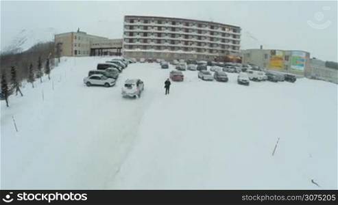 Aerial shot of a car driving to the outdoor parking area by the big hotel in winter day