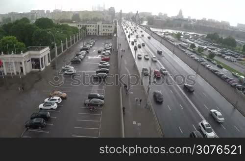 Aerial shot of car traffic on Krymsky Bridge, parking lots and people walking on sidewalk on nasty rainy day in Moscow, Russia