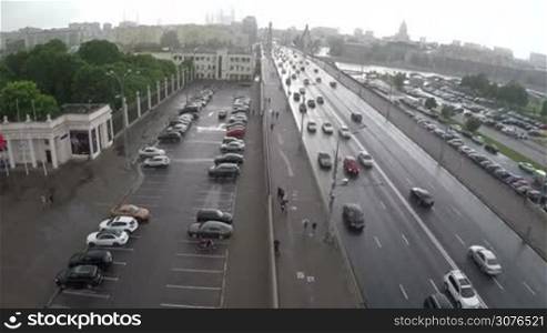 Aerial shot of car traffic on Krymsky Bridge, parking lots and people walking on sidewalk on nasty rainy day in Moscow, Russia