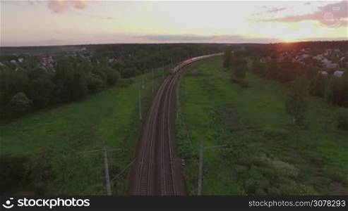 Aerial shot of cargo train running through the village in the woods at sunset, Russia