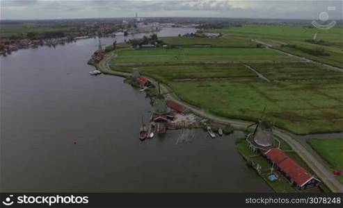 Aerial shot of Dutch village with view to the river, old windmills and green fields