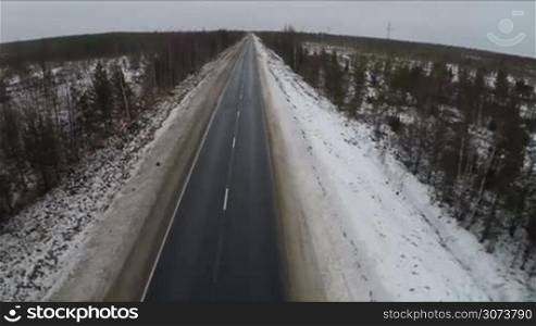 Aerial shot of empty road in winter. Vast northern snowy territories with rare trees and bushes