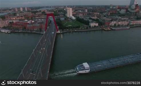 Aerial shot of evening Rotterdam, Netherlands. City view with Willem Bridge and empty barge sailing along the river