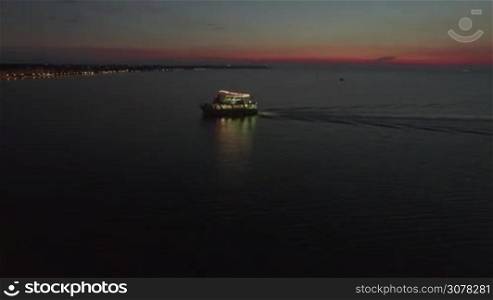 Aerial shot of illuminated touristic boat sailing in the sea near the shore at night. Water traveling in Thessaloniki, Greece