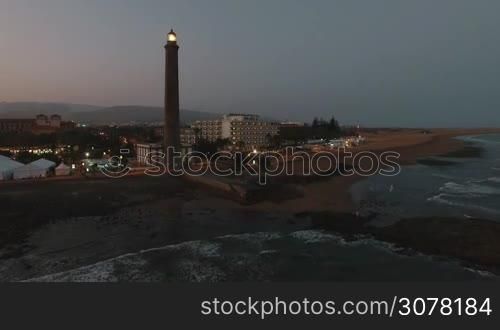 Aerial shot of Maspalomas Lighthouse with light in the dusk. Gran Canaria coast, Canary Islands