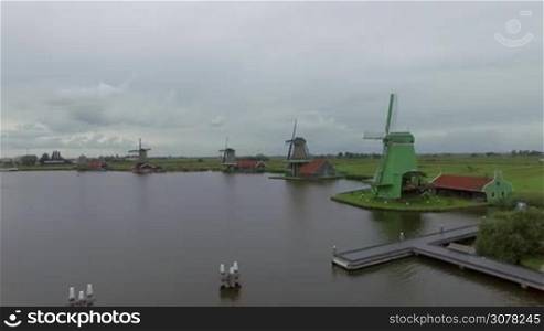 Aerial shot of old windmills on waterside and green fields. Village in Netherlands