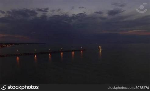 Aerial shot of quiet sea, pier and sailing touristic boat at night. Thessaloniki, Greece