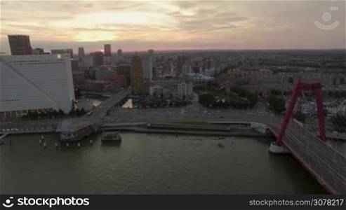 Aerial shot of Rotterdam at sunset, Netherlands. Waterside view of city buildings, Willem Bridge and transport traffic