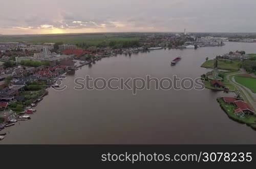 Aerial shot of ship sailing along the river flowing through the township in Netherlands. View at sunset