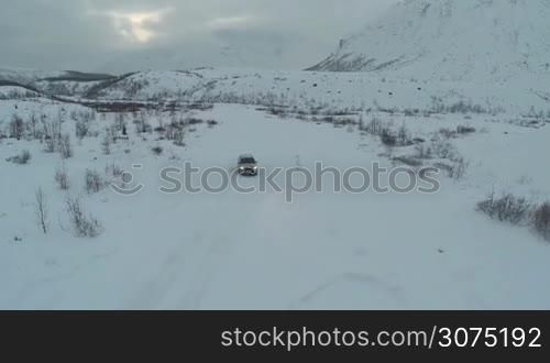 Aerial shot of silver car moving along the road through the field in deep snow