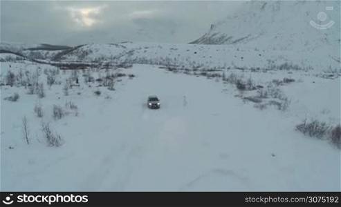 Aerial shot of silver car moving along the road through the field in deep snow