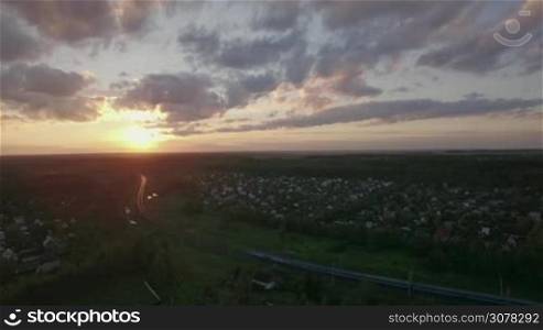 Aerial shot of summer scene with countryside and moving passenger train at sunset. Railway running through the village, Russia
