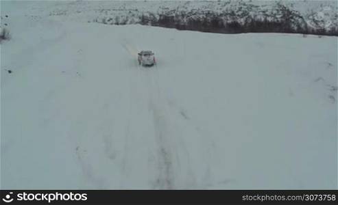 Aerial shot of the driving on winter snowy road in the countryside, back view
