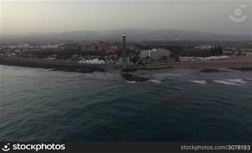 Aerial shot of the Gran Canaria resort and Maspalomas Lighthouse in the evening. Flying from the ocean to the beach