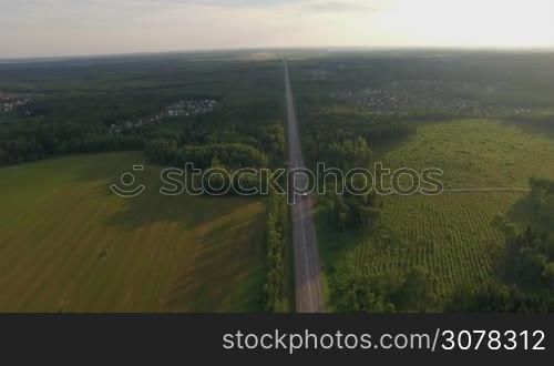 Aerial shot of the highway among the fields and woods near dacha communities, Russia
