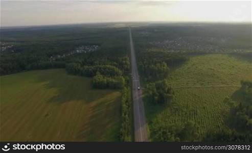 Aerial shot of the highway among the fields and woods near dacha communities, Russia
