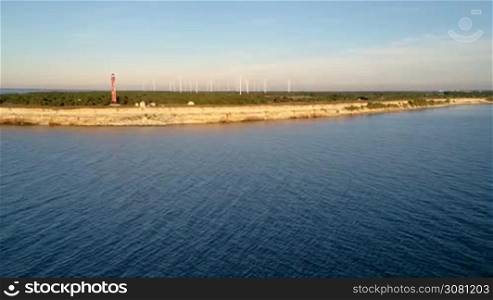 Aerial shot of the old lighthouse and the park of wind generators on the peninsula in summer at sunset