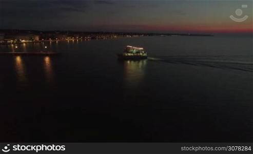 Aerial shot of touristic boat sailing to the pier after night sea tour. Thessaloniki, Greece