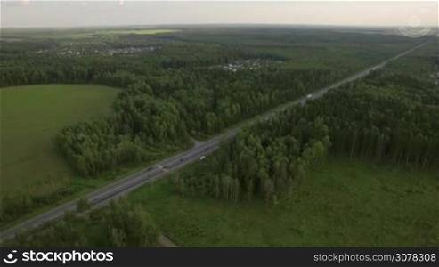 Aerial shot of transport traffic on the road in the countryside. Highway in the woods near the villages, Russia