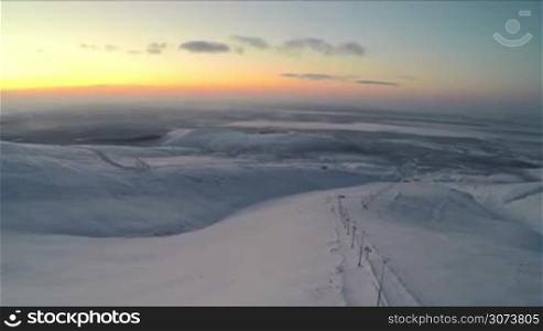 Aerial shot of vast territory of snowy hills and skiing run in Khibins, sky in warm evening colors. Kola Peninsula, Russia
