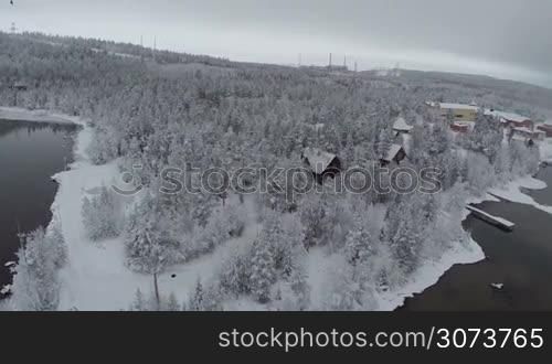 Aerial shot of winter camp located in pine wood in Finland. Snowy landscape with lakes