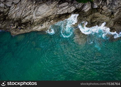 Aerial top view from drone of sea waves hitting rocks and small fishing man on island in Phuket, Thailand